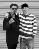 Two men posing for a photo in front of a metal shutter.