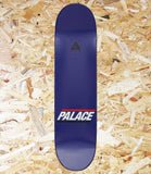 A dark blue skateboard deck with the Palace logo printed on the bottom, displayed flat on a background of shredded plywood.