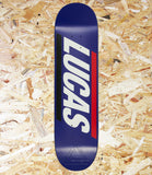 A skateboard deck with a dark blue background, featuring the brand name 'LUCAS' in large white letters with black and red side stripes, photographed from directly above on a wood chip background.
